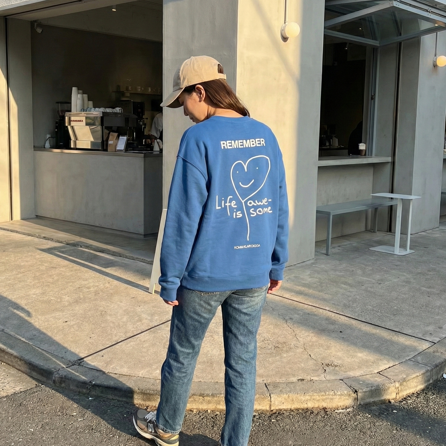 Blaues Unisex Sweatshirt von KOMM KLAR DIGGA mit Rückenprint „Life Is Awesome“, minimalistisches Herz-Design, lässiger Streetwear-Look im Alltag getragen.