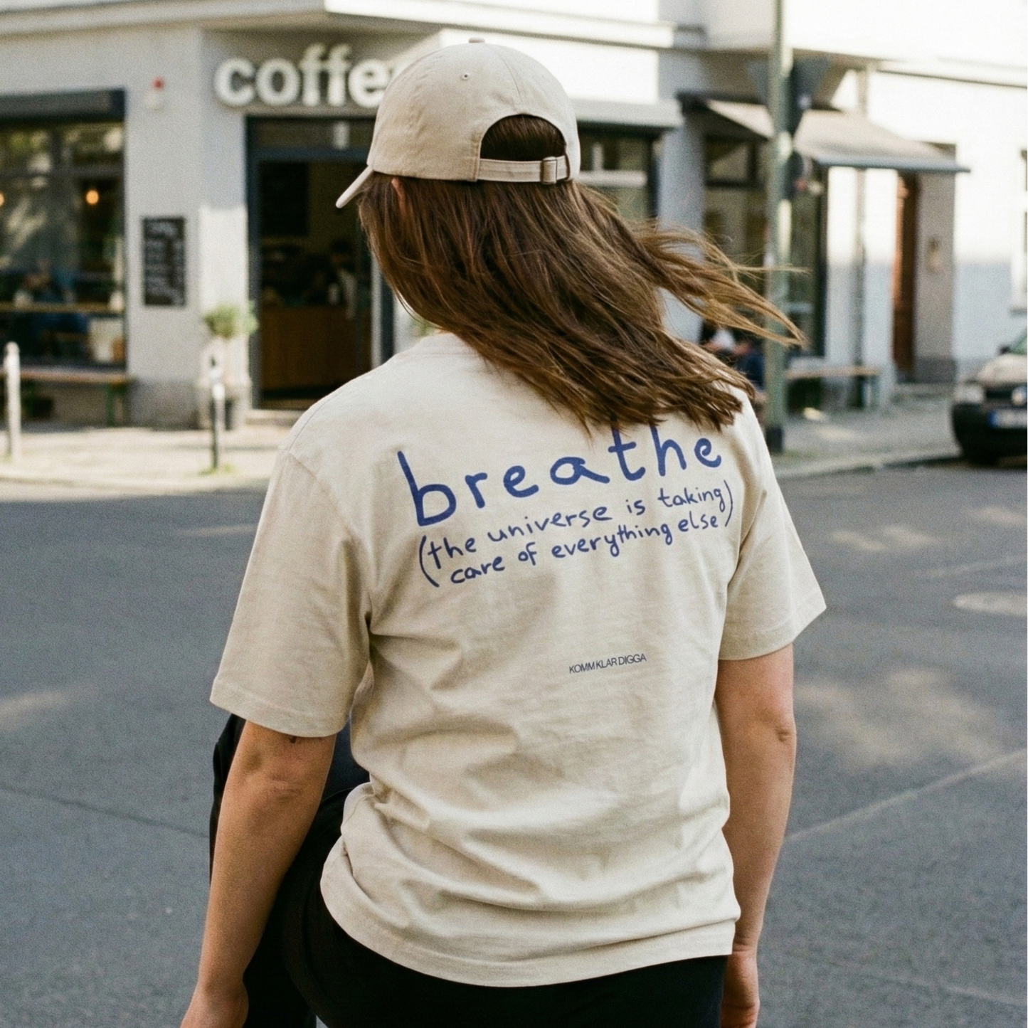 Beiges Heavy Unisex T-Shirt aus 100 % Bio-Baumwolle von KOMM KLAR DIGGA mit Rückenprint „breathe (the universe is taking care of everything else)“, ruhiger Streetwear-Look im urbanen Alltag.